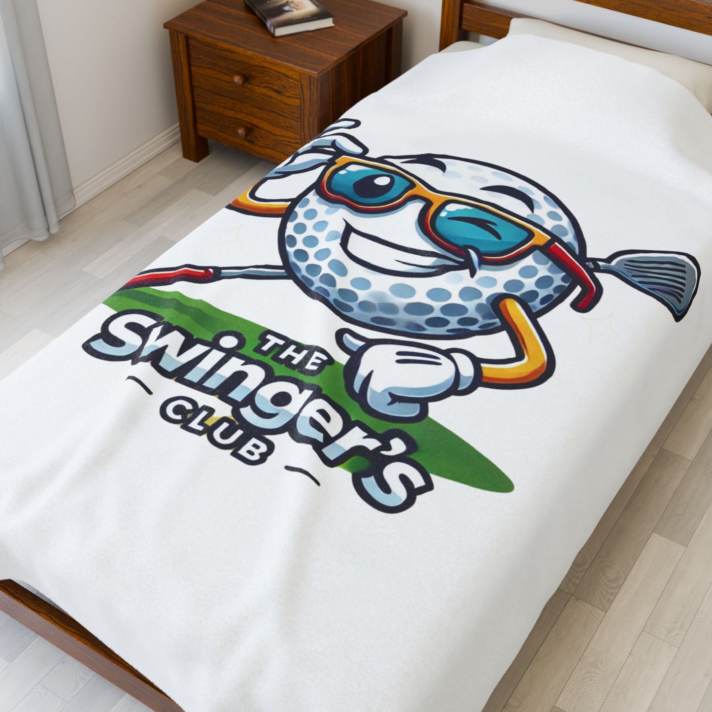 Blanket with cartoon character and 'The Swinger's Club' text on a bed in a room.