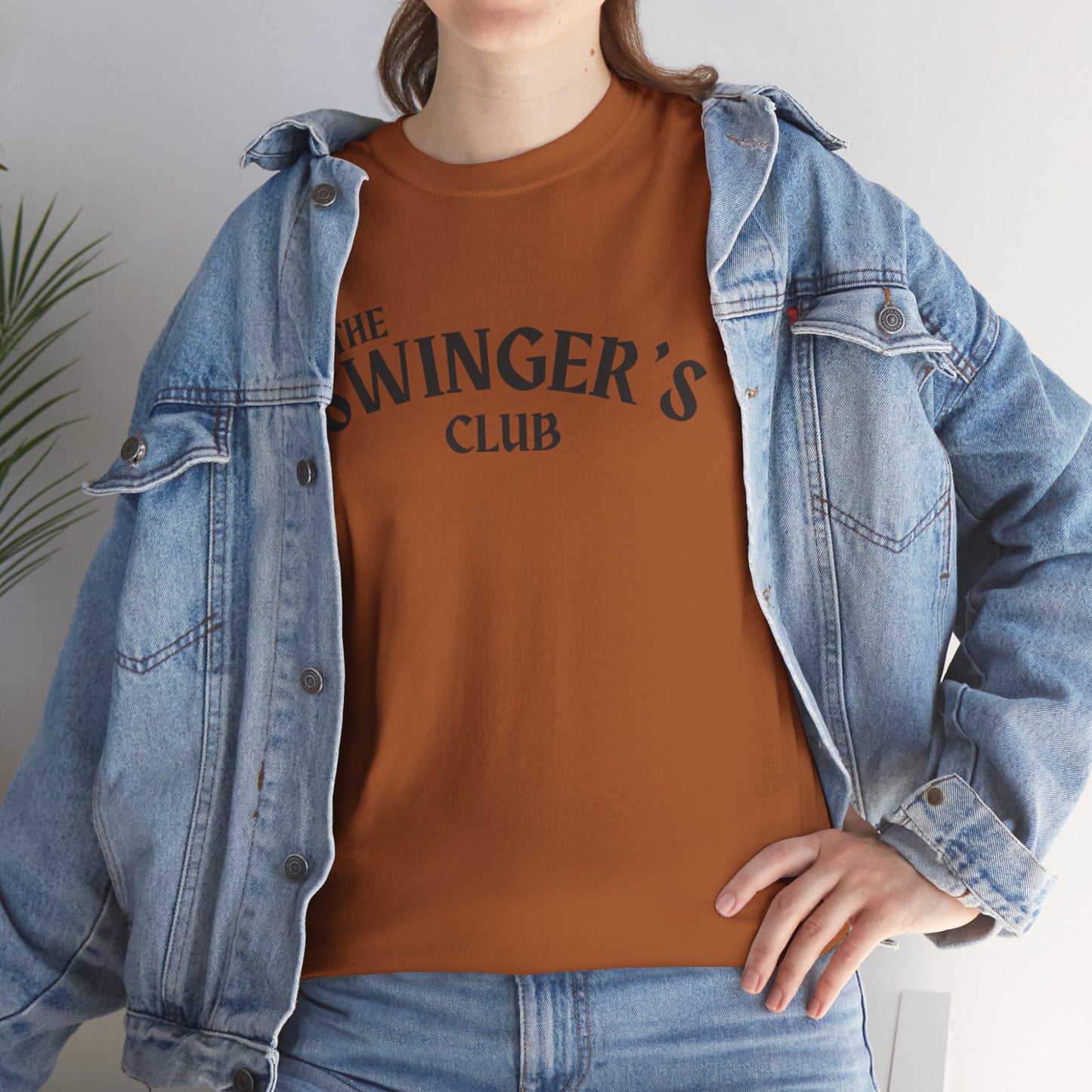 Person wearing a brown t-shirt with 'The Swinger's Club' text and a denim jacket.