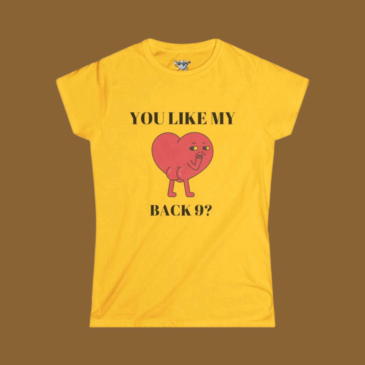 Yellow Women's shirt with a heart with a face and you can see it's backside. Above the design it says. "You Like My" and under the design "Back 9?" with a brown background