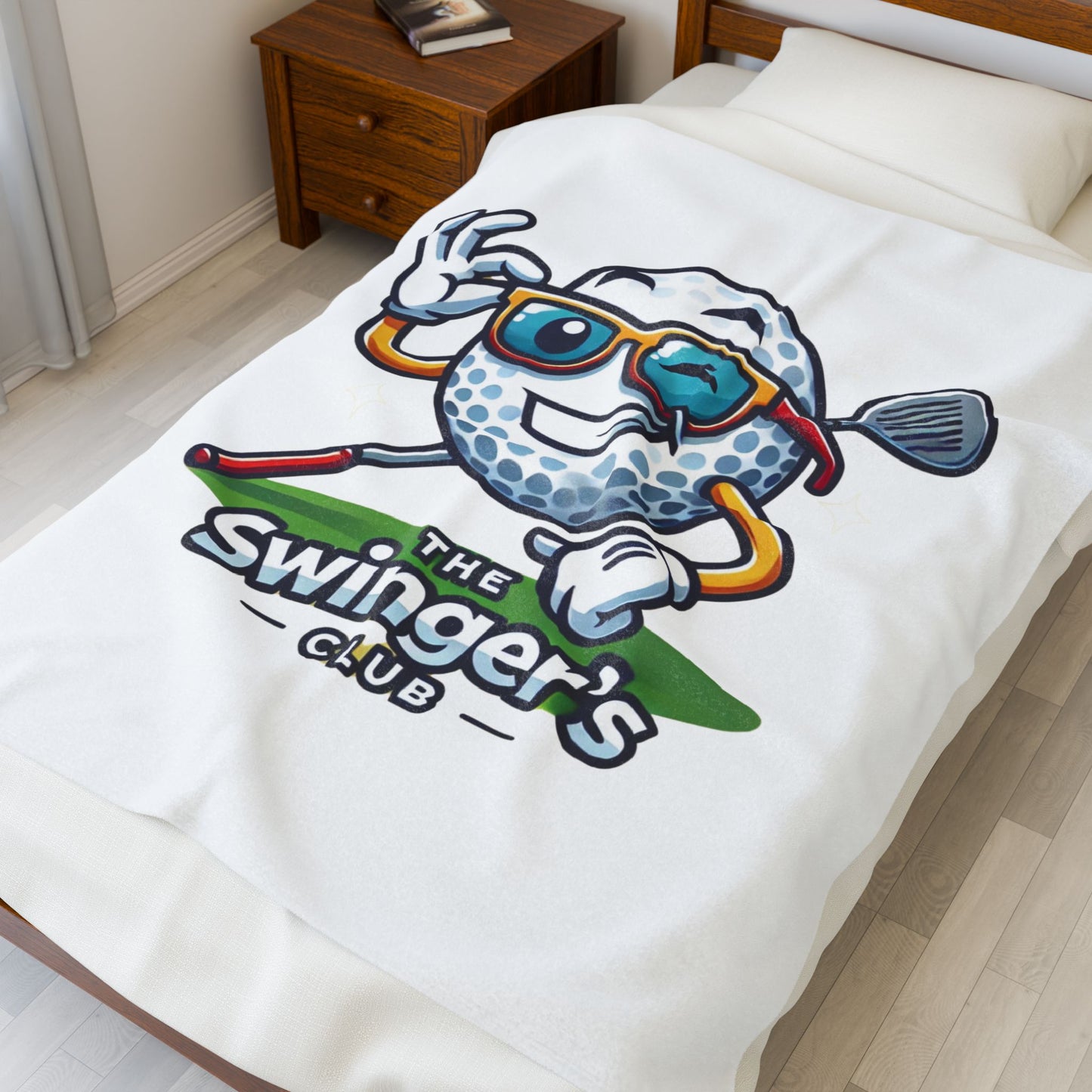 Blanket with a cartoon golf ball design and 'The Swinger's Club' text on a bed.